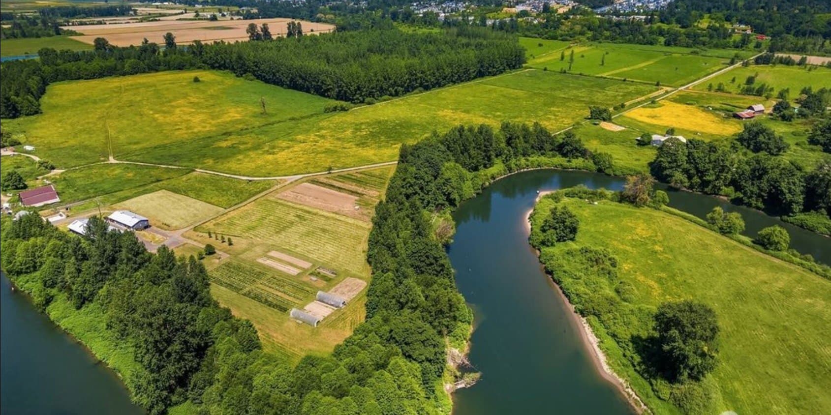 Aerial view of Wild Roots Farm in Duvall, WA — fields and pastures wrapped by a winding river, with woodland and outbuildings at the heart of the property